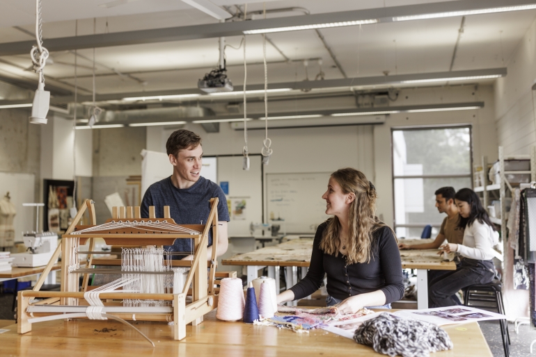A male student chats with a female student as he uses a weaver in the textile studio at UNSW Paddington campus.