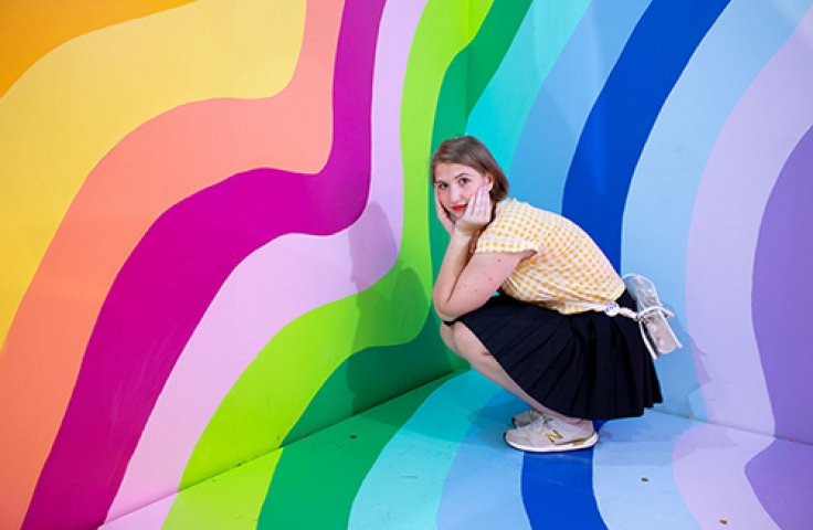 UNSW Arts & Social Science gradute Kayla Medica sitting infront of a colourful wall
