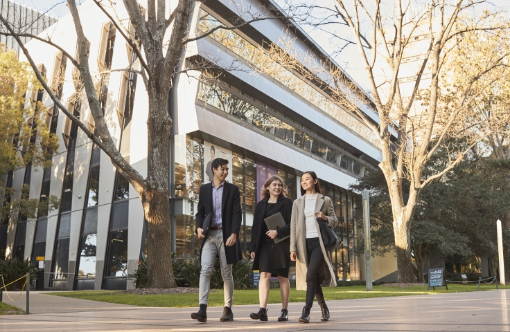 Three Law students walking on Main Wallkway with the Law Building in the background, dressed in smart attire and winter coats